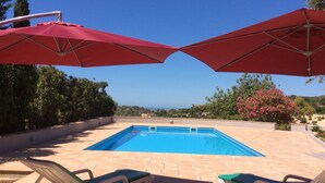 A rectangular outdoor pool with two red umbrellas and two lounge chairs. - 2 Bedroom, Fully Air-conditioned Country House With Large Private Pool (santa barbara de nexe)