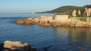 Paisagem costeira com rochas grandes e um muro de pedra à beira-mar.