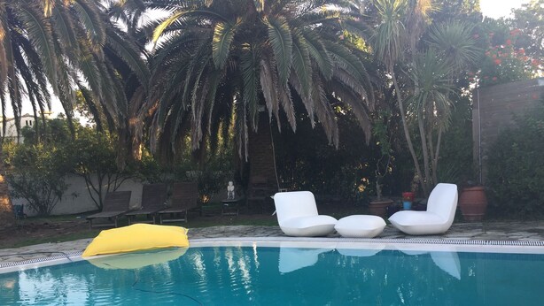 Piscina com espreguiçadeiras brancas e uma cobertura amarela.