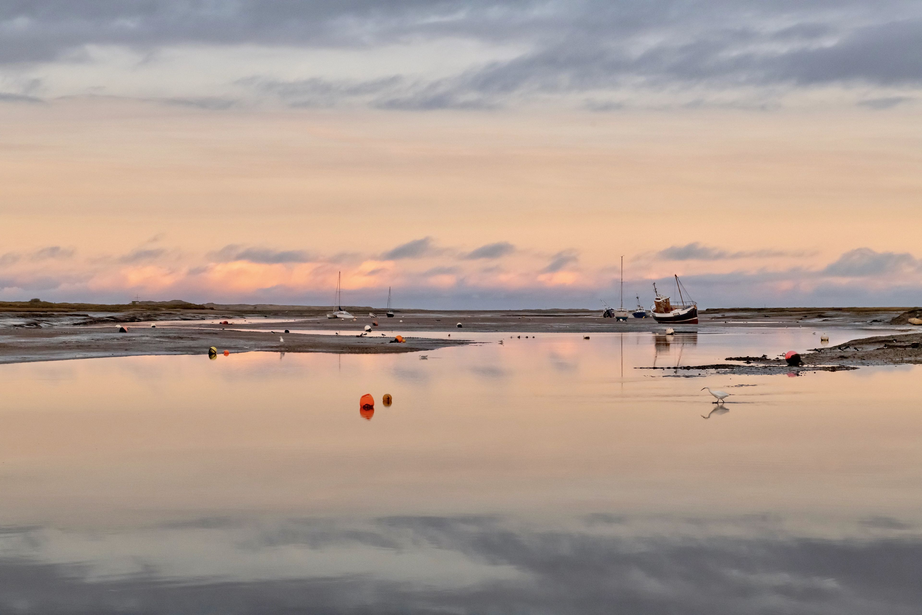 A calm waterfront with boats and a crane, reflecting the sky.