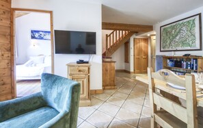 A living room with a television, wooden furniture, a bookshelf, and a staircase leading to another room. - Apartment Apollo 7p/3r (Les Houches)