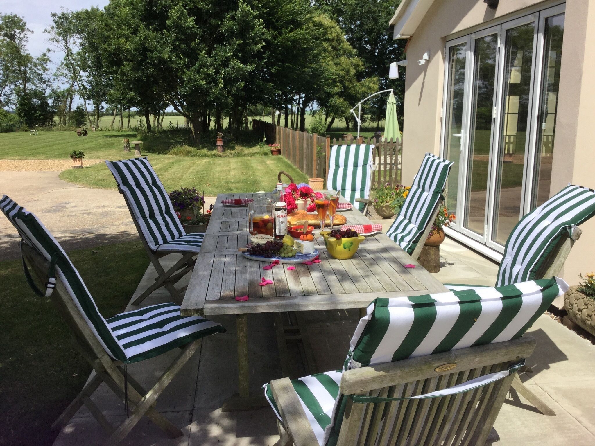 A wooden patio table with striped chairs, a pitcher of drinks, and a fruit bowl.