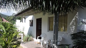 A white building with a door, windows, and a small porch area with white plastic chairs.