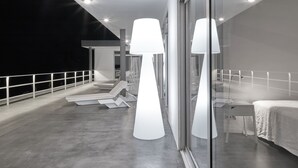 Une chambre d’hôtel moderne dotée d’une grande fenêtre en verre, d’un balcon avec une balustrade et d’un lit recouvert d’une courtepointe blanche.