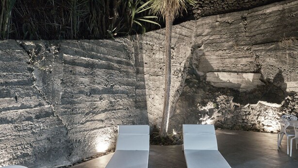 Un espace de détente extérieur moderne, avec deux fauteuils blancs et une petite table, adossé à un mur de pierre et entouré de verdure.