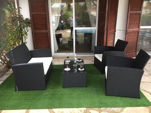 A patio area with black wicker furniture, a small table with glasses and a bottle, and a glass door leading to a pool. -  Villa Lamda A Beautiful Modern Bungalow in Tranquil Peaceful Pissouri Village. (Pissouri)
