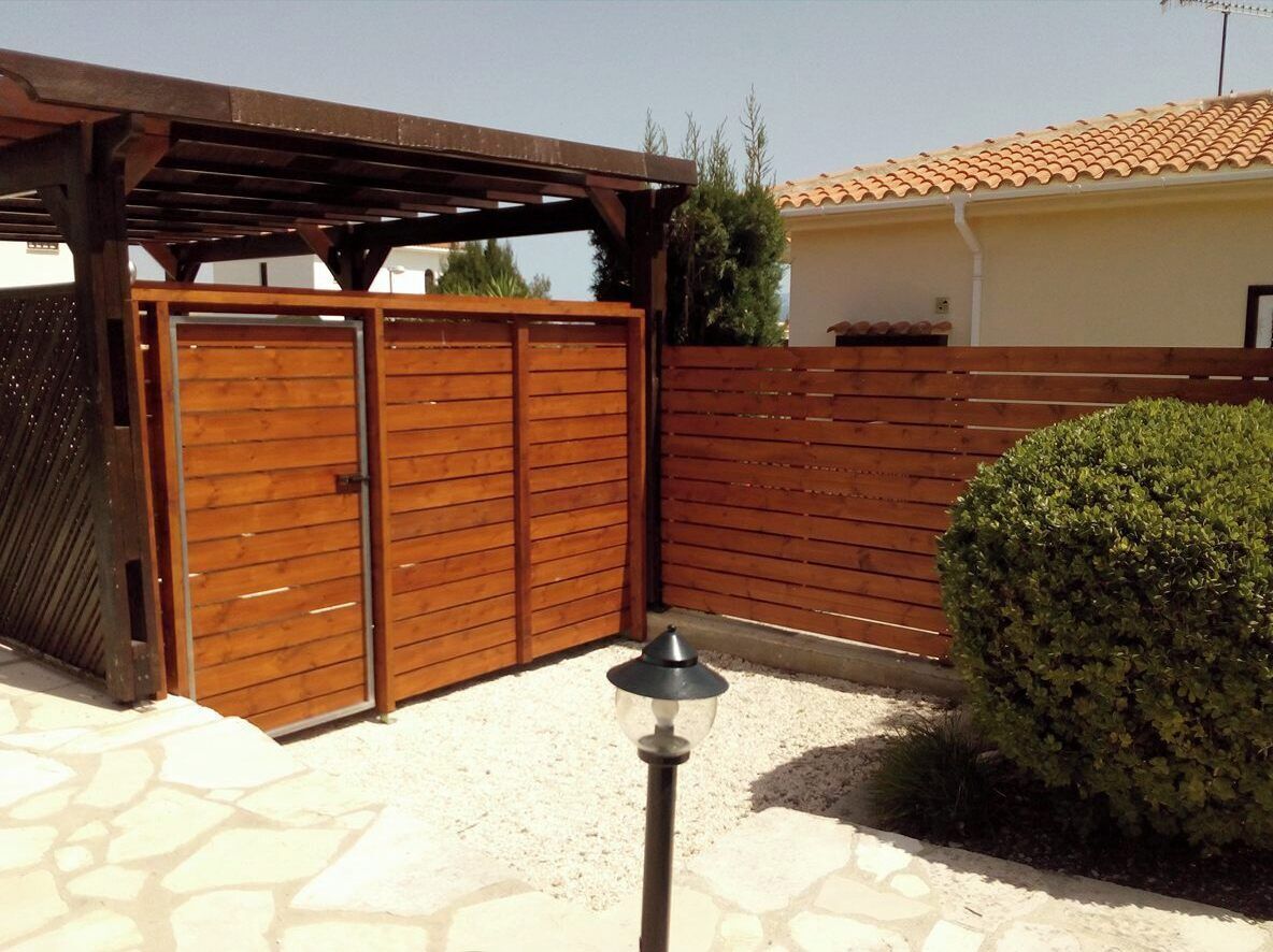 A gated outdoor area with a wooden fence, a pergola, and a well-maintained hedge.