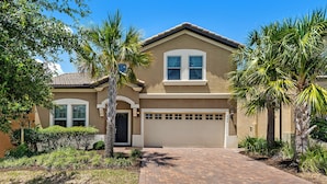 A two-story house with a beige exterior, a garage, and a brick driveway.