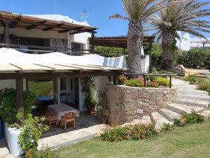 A house with a covered patio, stone steps, and a garden with flowers and a palm tree. - House with garden (Villasimius)