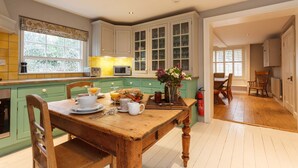 Une cuisine spacieuse avec des meubles de couleur verte, une table à manger en bois et une vue sur l’espace repas.