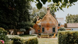 Une maison de campagne en briques, dotée d’un toit à pente, entourée d’une végétation luxuriante et d’un jardin bien entretenu.
