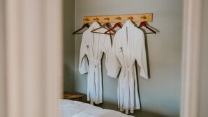 Une pièce comprenant un portant en bois sur lequel sont suspendues des robes blanches, un tabouret en bois et un lit avec du linge de lit blanc.
