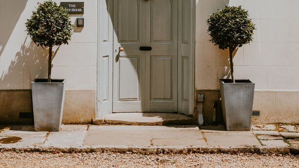 Un bâtiment à la façade blanche, doté d’une grande porte d’entrée en arc de cercle et de deux plantes en pot de chaque côté.