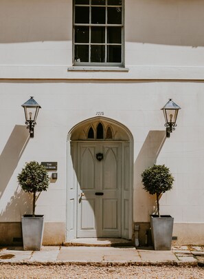 A building with a white facade, a large arched entrance door, and two potted plants on either side. - The Gate House - Wimborne, Dorset (Wimborne)