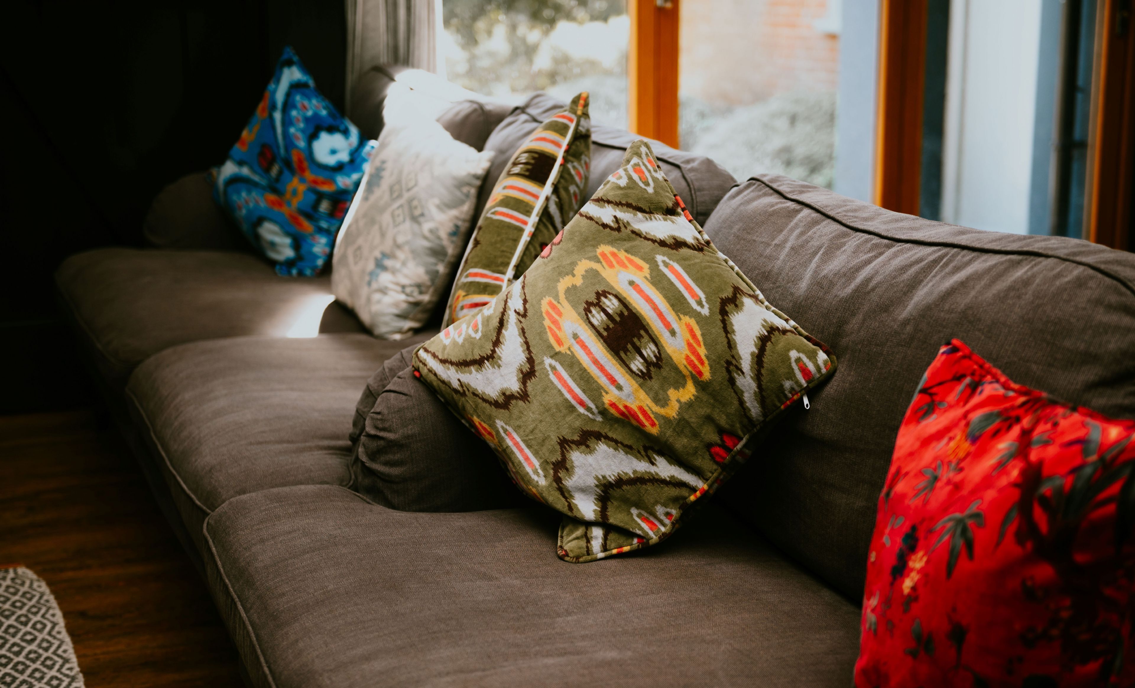 Ein braunes Sofa mit mehreren Kissen, darunter eines gemusterten und eines roten.