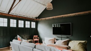 Un salon moderne avec un grand canapé d’angle gris, une table basse en bois et un téléviseur fixé au mur.