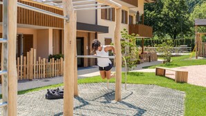 A gym area with a pull-up bar, wooden deck, and a building with balconies in the background. - Residence Toli Pool with outdoor heated Pool 30° (Ledro)