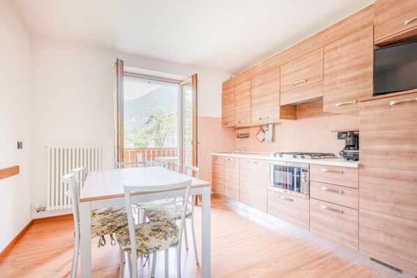 Ett modernt kök med träskåp, ett matbord med stolar och ett stort fönster som erbjuder en utsikt över grönområden och berg.