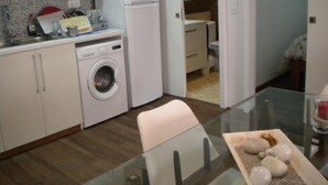 Eine kompakte Küche mit Waschmaschine, Kühlschrank und Essecke mit Glastisch.