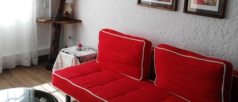 Ein Wohnzimmer mit einem roten Sofa, Holzregalen und gerahmten Kunstwerken an der Wand.