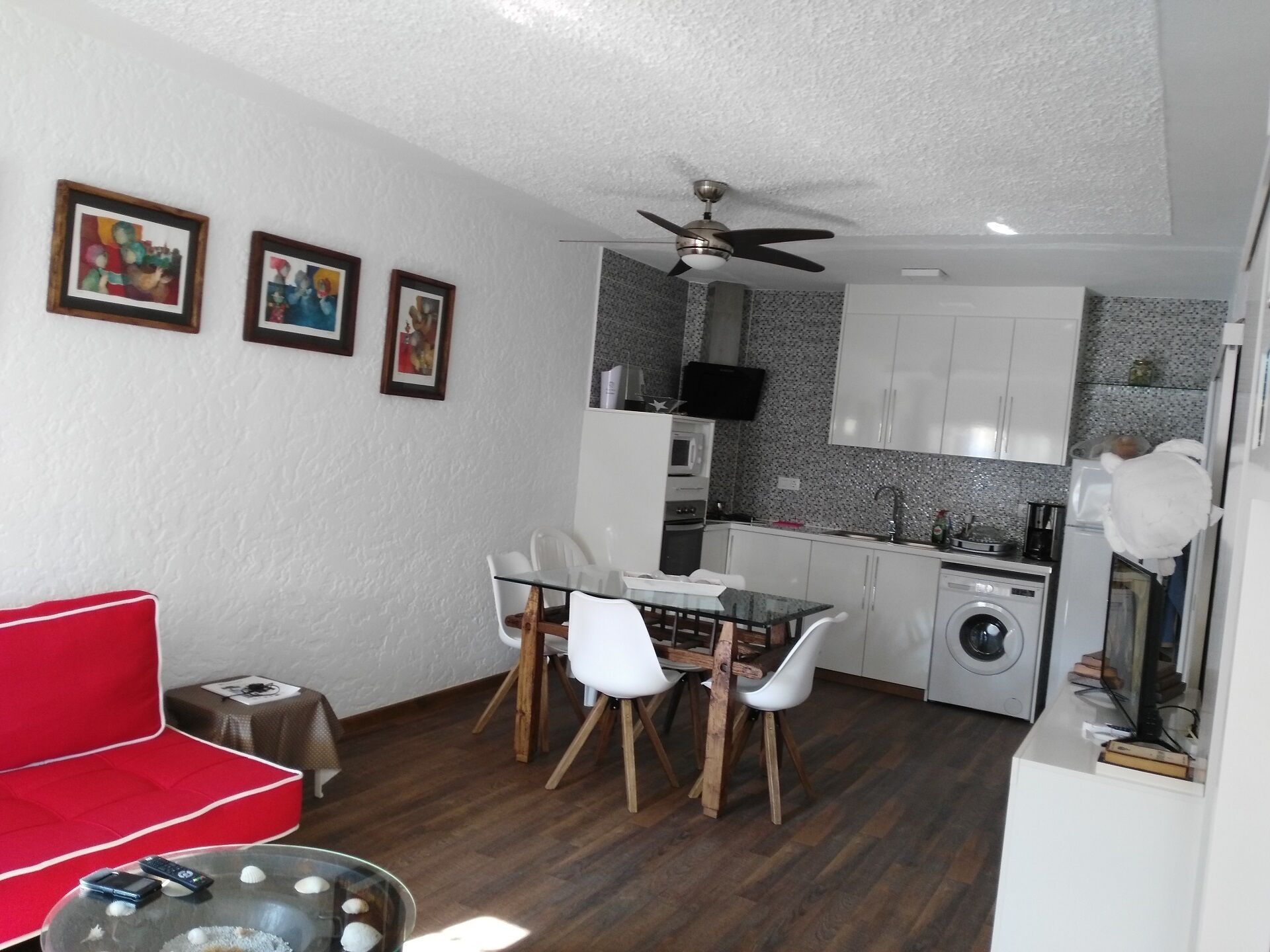 A compact living space with a kitchenette, a dining area with a glass table, and a red sofa.