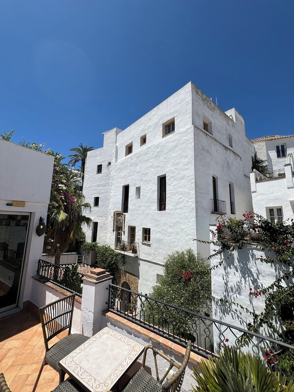 A white building with multiple windows and balconies, surrounded by greenery and a tiled patio area. - Beautiful Moorish Town House with Private Pool, Roof Terrace, 3 beds/2 bathrooms (Vejer de la Frontera)