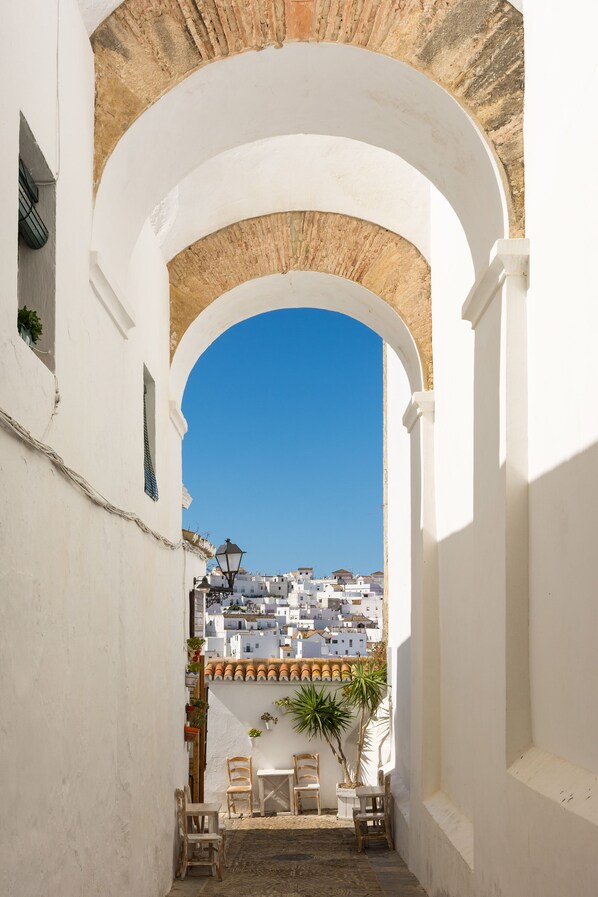 Un portail en arc donne accès à une cour d’où l’on aperçoit, au loin, des bâtiments blancs.