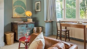 A cozy room with a wooden table, a leather sofa, a small round table with glasses, a lamp, a map on the wall, and a window with curtains. - Station House, Helhoughton, Norfolk (Helhoughton)