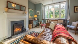 A cozy living room with a fireplace, leather sofa, and a large window with curtains. - Station House, Helhoughton, Norfolk (Helhoughton)