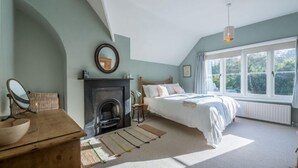 A bedroom with a bed, a fireplace, a mirror, and a window. - Station House, Helhoughton, Norfolk (Helhoughton)