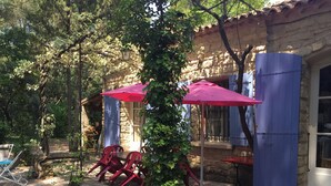 A rustic outdoor seating area with stone walls, red chairs, and a blue umbrella.