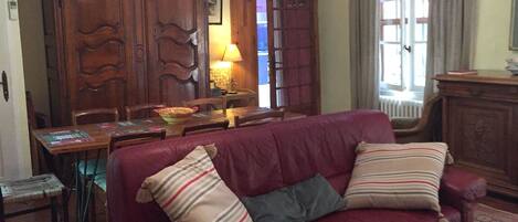 Una sala de estar con un sofá rojo, dos almohadas, un aparador de madera, una mesa y una araña.