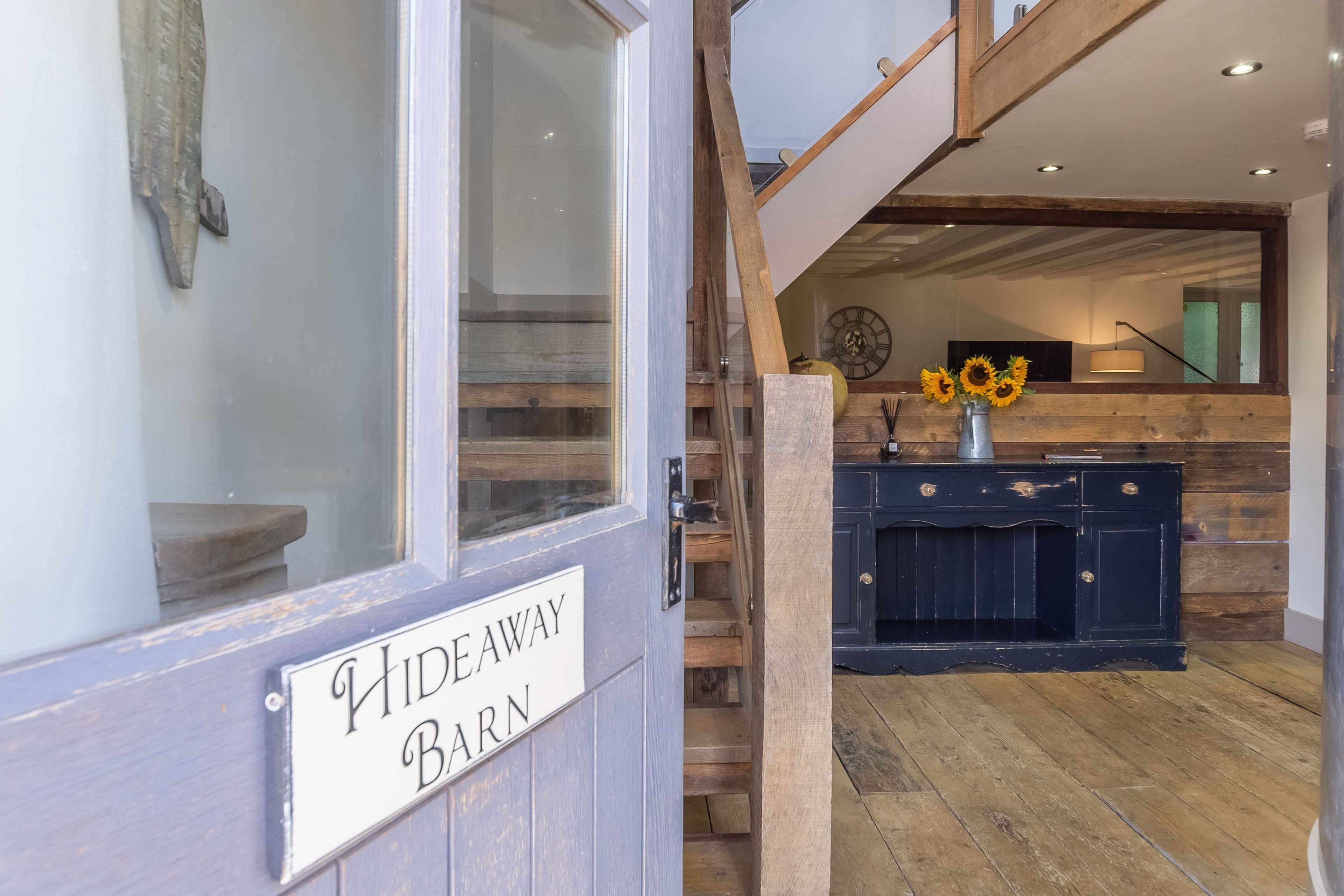 A wooden staircase leading to a loft area with a rustic decor, including a clock and a vase with sunflowers.