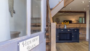 A wooden staircase leading to a room with a rustic decor, including a black cabinet and a vase of sunflowers. - Hideaway Barn, Thornham, Norfolk (Thornham)