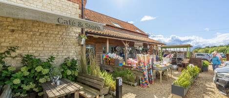 A café & store with outdoor seating, a brick wall, and a tiled roof.