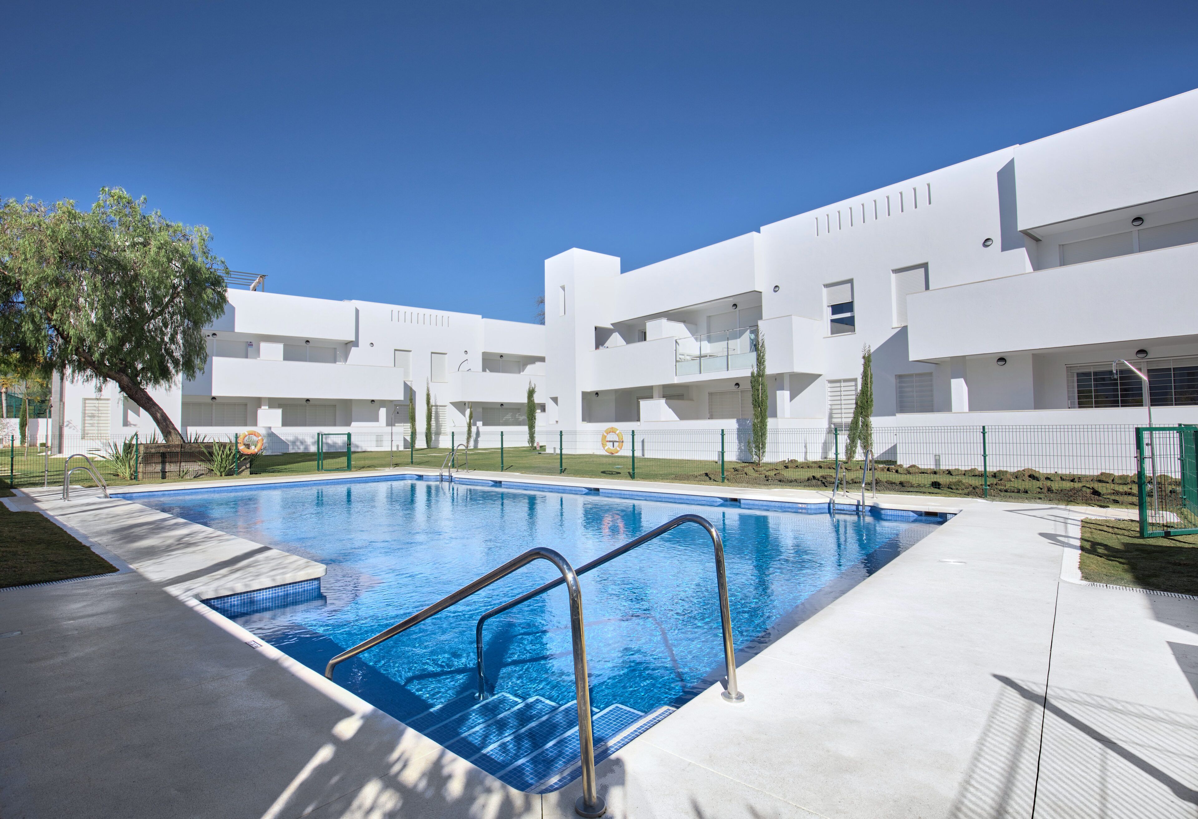 Un bâtiment moderne doté d’une piscine, entouré d’une pelouse bien entretenue et surplombé d’un ciel bleu azur.