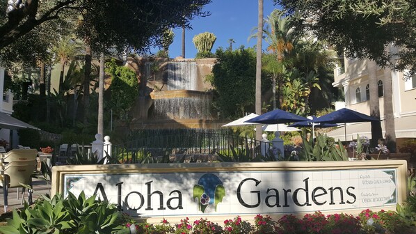 Señal de Aloha Gardens con una cascada y zona de estar al aire libre.