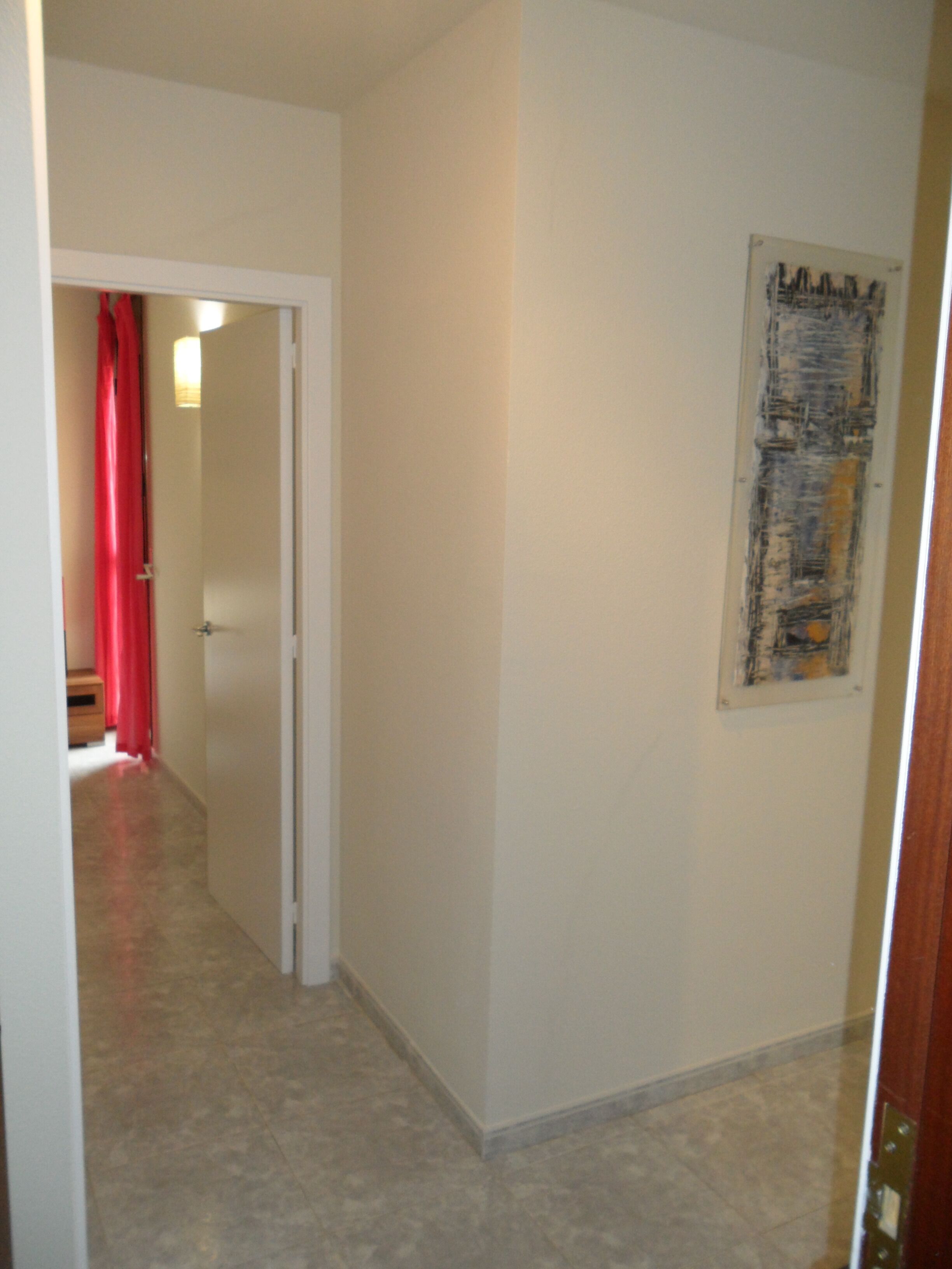 A hallway with a door leading to a room, a red curtain, and a painting on the wall.