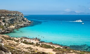 A coastal area with a rocky cliff, clear turquoise waters, and a boat in the distance.