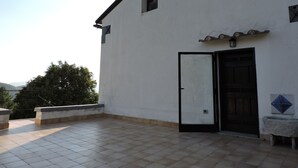 A white building with a tiled patio, a black door, and a small window.
