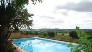 Une piscine rectangulaire à l’eau d’un bleu limpide, entourée d’un petit muret en pierre et dotée d’une échelle en métal.