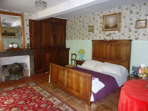 Ein traditionell eingerichtetes Schlafzimmer mit einem hölzernen Bett, einem Nachttisch, einem Sessel, einem Spiegel und einem Kamin.
