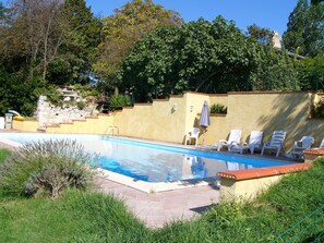Ein Pool mit Steinmauer, einer Rasenfläche und einigen weißen Liegestühlen.