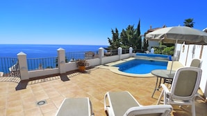 Une piscine sur le toit offrant une vue sur la mer, entourée de chaises longues et d’une table.