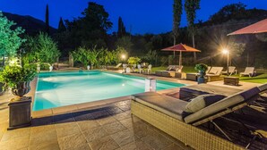 A rectangular swimming pool with a stone deck, surrounded by lounge chairs and umbrellas, set against a backdrop of trees and a night sky. - Tuscan Fairytale Family Villa close to Beaches and Lucca (Camaiore)