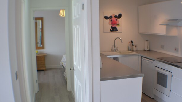 A modern kitchen with white cabinets, a sink, and a stove. There is a door leading to another room. - Why book a room when you can have a suite (Wootton)