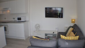 A modern living room with a grey sofa, a flat-screen TV, and a white desk with a fan. - Why book a room when you can have a suite (Wootton)