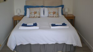 A neatly made bed with a white bedspread and blue pillows, two bedside tables with lamps, and a grey curtain. - Why book a room when you can have a suite (Wootton)
