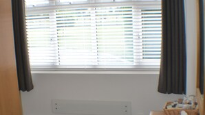 A room with a window covered by blinds, a wooden bench, and a small wooden table with a basket. - Why book a room when you can have a suite (Wootton)