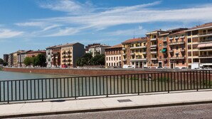 Vista del río de una hilera de edificios de varios pisos con balcones, un sendero pavimentado y una barandilla de metal.